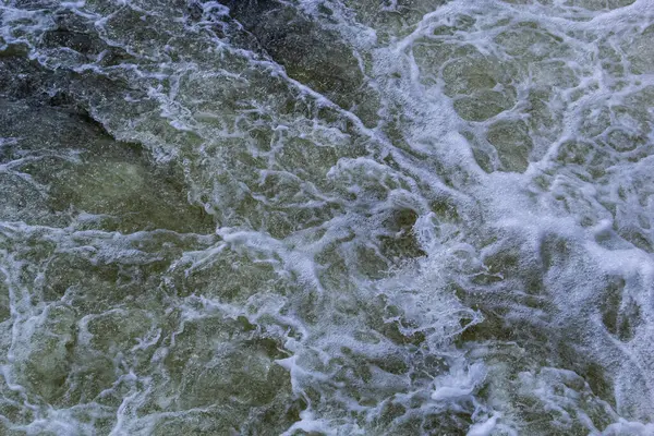テクスチャーされた背景を形成するきれいな深緑色の川からの激しい白い川の流れの詳細を閉じます ストック写真