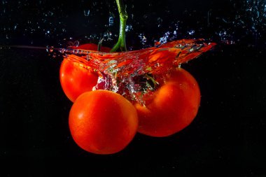 Fresh red tomato falling into water with water splash and air bubbles isolated on black background. clipart