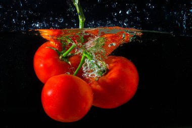 Suya düşen taze kırmızı domates. Su sıçraması ve siyah arka planda izole edilmiş hava kabarcıkları..