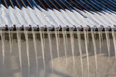 Keskin buz saçakları ve çatıdan sarkan erimiş kar. Güzel şeffaf buz saçakları yavaşça bir çatının üzerinde süzülüyor..