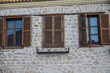 Büyüleyici taş duvarda, Arnavutluk 'un kültür mirası ve mimari güzelliğini yansıtan ahşap panjurlar ve dövülmüş demir bir balkon yer alıyor..