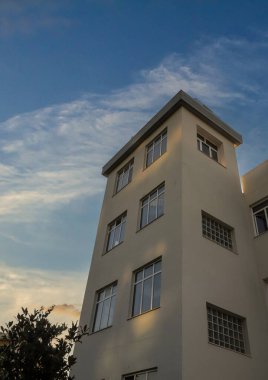 Bina, günbatımının sıcak tonlarını yansıtan büyük pencereler ve minimalist bir tasarıma sahip. Yakınındaki ağaçların yüzeyinde ilginç gölgeler var..