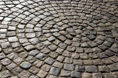 Tarihi bir kasabada düzensiz taşlarla yaratılmış girdap gibi dönen bir kaldırım taşı tasarımı hem sanatsal hem de eskimiş güzelliği yumuşak güneş ışığı altında yansıtıyor..