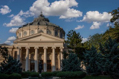 İzleyiciler, hoş bir öğleden sonra Bükreş 'teki Romanya Atinası' nın parlak mavi gökyüzünün altındaki karmaşık klasik tasarımını takdir etmek için toplandılar..
