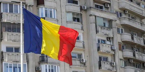 Bükreş 'te rüzgarda dalgalanan Romen bayrağı, açık bir günde kentsel konut arkaplanlarına karşı canlı renkleri vurguluyor.