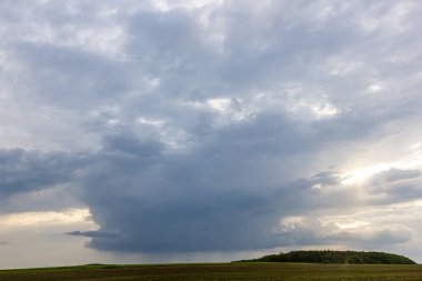 Gün batımında yemyeşil bir tepenin üzerinde kara bulutlar belirir, gölgeler bırakır ve muhtemel yağmurun sinyalini verir. Atmosfer gergin ve dramatik..