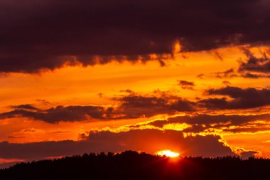 Güneş ufkun altına batıyor, bulutlar huzurlu bir akşam boyunca gökyüzünü turuncu ve mor tonlarıyla doldururken, dağlar boyunca sıcak ışık saçıyor..