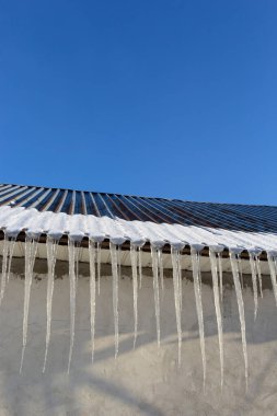 Keskin buz saçakları ve çatısından sarkan erimiş kar. Güzel şeffaf buz saçakları yavaşça bir çatının üzerinde süzülüyor..