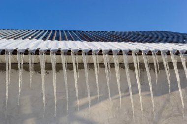 Keskin buz saçakları ve çatıdan sarkan erimiş kar. Güzel şeffaf buz saçakları yavaşça bir çatının üzerinde süzülüyor..