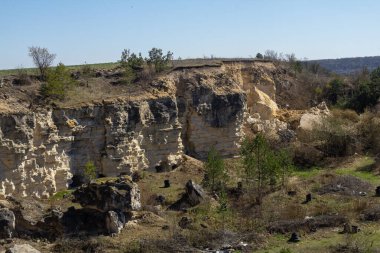 Kayalık bir uçurum, güpegündüz doğal erozyonu aydınlatan çimen ve küçük ağaçlarla çevrili yıpranmış taş tabakalarını sergiliyor..