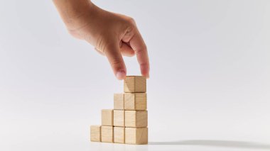 Yakından çekilen el, tahta küpleri merdiven şeklinde istifliyor. Beyaz arka plan üzerine sembol veya logo, iş büyümesi ve yönetim konsepti oluşturmak için model alınıyor.