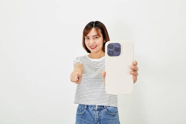 Tişörtlü ve kot pantolonlu genç Asyalı kadın akıllı telefon gösteriyor.