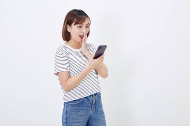 Güzel Asyalı genç iş kadını kısa esmer kadın elinde akıllı bir telefon görüşmesi tutarak cep telefonundaki bilgilere tepki veriyor. Beyaz arka planda güvenle gülümseyen neşeli yüz ifadesi stüdyosu.