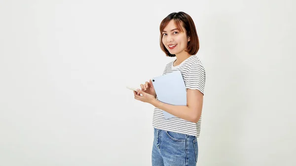 Tシャツとジーンズを身に着けている短い茶色の髪を持つ魅力的な若いアジアの女性従業員笑顔と白い背景コピースペースに立ってスマートフォンやデジタルタブレットを保持 — ストック写真