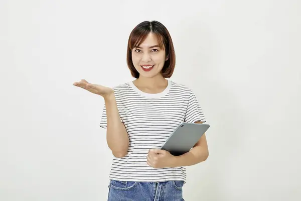 Tシャツとジーンズを身に着けている短い茶色の髪と魅力的な若いアジアの女性従業員は笑顔と白い背景コピースペースに立ってデジタルタブレットを保持 — ストック写真