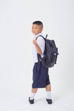 Tayland okul üniforması içinde sırt çantası ve beyaz arka planda bir kitapla duran yakışıklı bir Asyalı çocuk. Okula geri dön.
