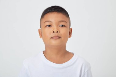 Cute smiling Asian boy in a plain white t-shirt looking at the camera in an isolated studio light white color background clipart