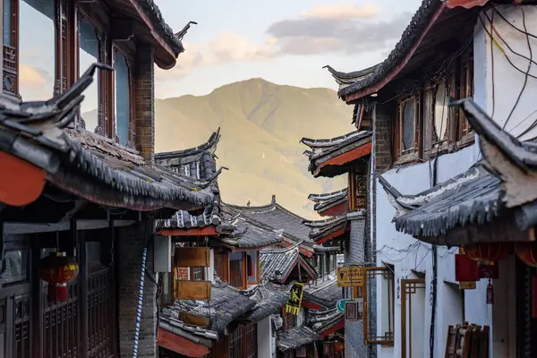 Lijiang, Yunnan Eyaleti, Çin - 23 Ekim 2015: Eski Lijiang kasabasındaki otantik evlerin geleneksel Çin siyah kiremit çatılarının muhteşem manzarası. Manzaralı dağlar gün batımında görülebilir..