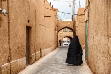 Siyah çarşaf giyen İranlı bir kadın tarihi Yazd şehrinin dar caddesinde yürüyor. Antik şehrin eşsiz Pers mimarisi.