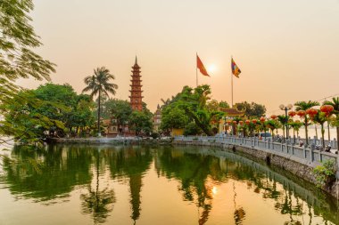 Hanoi, Vietnam - 19 Nisan 2019 Tran Quoc Pagoda ve Batı Gölü 'nün inanılmaz günbatımı manzarası. Vietnam bayrağı (altın yıldızlı kırmızı bayrak) ve Vietnam Budist bayrağı gölün üzerinde dalgalanıyor.