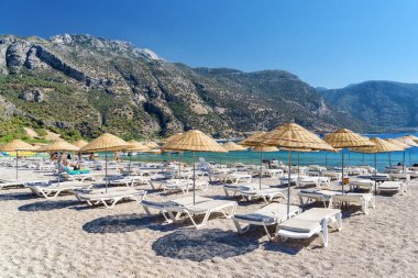 Türkiye 'nin Oludeniz Sahili' ndeki plaj şemsiyeleri ve güneş panzelerinin manzarası. Harika dağlar arka planda görülebilir. Oludeniz, Türkiye 'de popüler bir turizm merkezi..