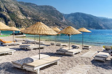 Türkiye 'nin Oludeniz Sahili' ndeki plaj şemsiyeleri ve güneş panzelerinin manzarası. Harika dağlar arka planda görülebilir. Oludeniz, Türkiye 'de popüler bir turizm merkezi..