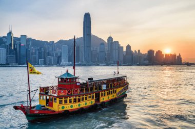 Hong Kong - 21 Ekim 2017 Victoria Limanı 'ndan gün batımında geçen bir turist teknesi. Şehir merkezindeki gökdelenlerin muhteşem manzarası. Hong Kong Adası silueti. Hong Kong Asya 'nın popüler bir turistik beldesidir..