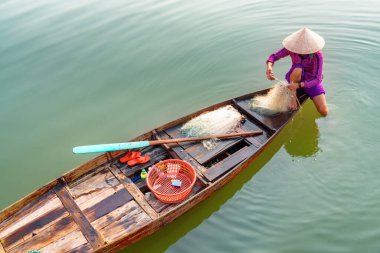 Vietnam 'daki Hoi An Kasabası' ndaki Thu Bon Nehri 'ndeki balık ağını kontrol eden geleneksel bambu şapkalı Vietnamlı kadın. Hoian Asya 'nın popüler bir turizm merkezidir..