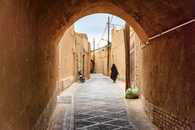 Siyah çarşaf giyen İranlı bir kadın tarihi Yazd şehrinin dar caddesinde yürüyor. Antik şehrin eşsiz Pers mimarisi.