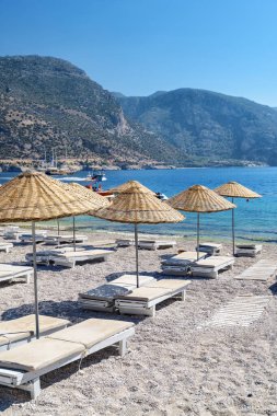 Türkiye 'nin Oludeniz Sahili' ndeki plaj şemsiyeleri ve güneş panzelerinin manzarası. Harika dağlar arka planda görülebilir. Oludeniz, Türkiye 'de popüler bir turizm merkezi..