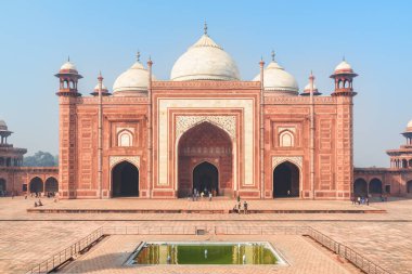 The Kau Ban Mosque of the Taj Mahal complex on blue sky background in Agra, India. Amazing red sandstone building reflected in water of pool. Wonderful Mughal architecture. clipart