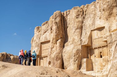 Shiraz, Iran - 31 October, 2018: Group of tourists at ancient necropolis Naqsh-e Rustam. Large tombs belonging to Achaemenid kings carved out of rock face at considerable height above the ground. clipart