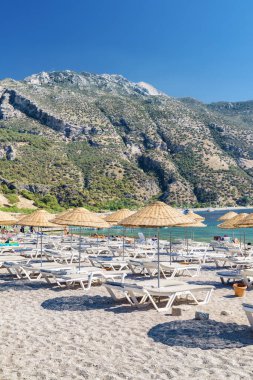 Türkiye 'nin Oludeniz Sahili' ndeki plaj şemsiyeleri ve güneş panzelerinin manzarası. Harika dağlar arka planda görülebilir. Oludeniz, Türkiye 'de popüler bir turizm merkezi..