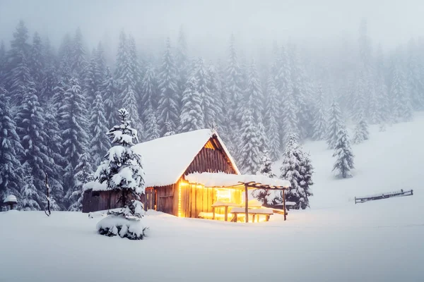 雪の森の中に輝く木造キャビンと幻想的な冬の風景 カルパチア山脈の居心地の良い家 クリスマス休暇のコンセプト — ストック写真