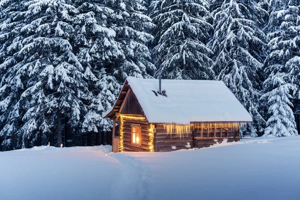 雪の森の中に輝く木造キャビンと幻想的な冬の風景 カルパチア山脈の居心地の良い家 クリスマス休暇のコンセプト — ストック写真