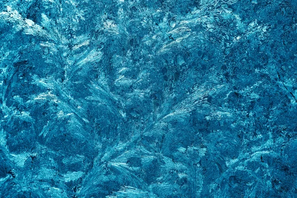 Christmas background with frozen pattern on window glass. Real blue texture of winter snowfrost