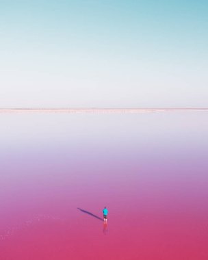 Mavi elbiseli yalnız bir adam yaz günü açık mavi gökyüzünün altında pembe göl suyunda çırpınıyor. Yaratıcı renk kavramı