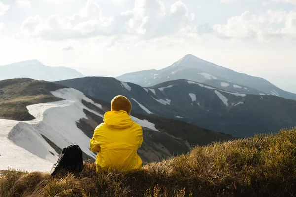 観光客は山の頂上の端に座っている 背景に雪のある日当たりの良い山 風景写真 — ストック写真