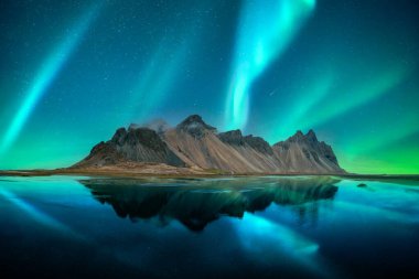 Aurora borealis kuzey ışıkları Vestrahorn Burnu 'ndaki ünlü Stokksnes dağlarının üzerinde. Gökyüzünün arka planındaki berrak suda yansıma, İzlanda. Peyzaj fotoğrafçılığı