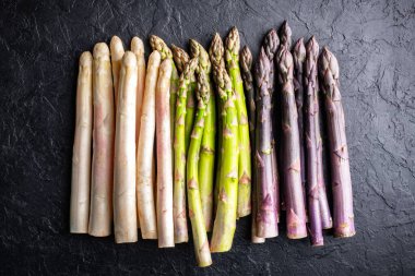 Top view of green, purple and white asparagus sprouts on black background closeup. Food photography clipart