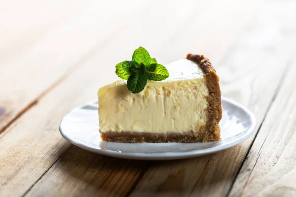 一片经典的纽约芝士蛋糕和薄荷糖放在木制桌子上的盘子里 面包店和甜饼甜点的概念 — 图库照片