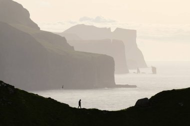 Kalsoy Adası 'ndan görülen Eysturoy ve Streymoy Adaları' ndaki ünlü Risin og Kellingin kayaları ve uçurumlarının arka planında insan silueti. Faroe Adaları, Danimarka. Peyzaj fotoğrafçılığı