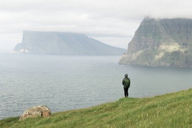 Küçük göl kenarındaki yalnız turist, Danimarka 'nın Faroe Adaları' ndaki Kalsoy adasından Atlantik Okyanusu 'ndaki sisli adalara bakar. Peyzaj fotoğrafçılığı