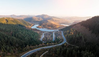 Sonbahar dağları dağ yolu yılanı, nehir ve karışık ormanlı panorama. Hava aracı görüntüsü. Peyzaj fotoğrafçılığı