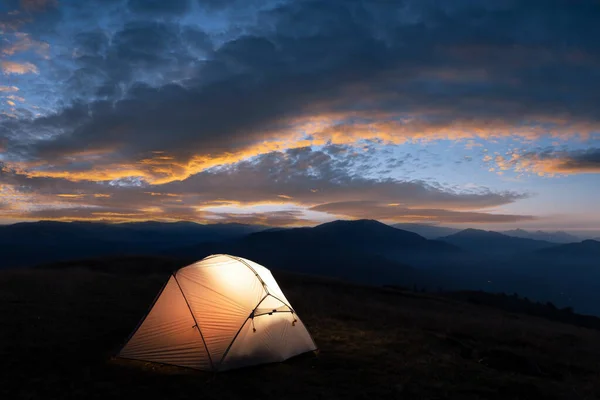 夏の山で信じられない夜 オレンジ色の夕日空の背景から内側から照らされたテント付きの観光キャンプ — ストック写真