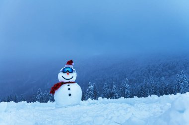 Kayak camlı komik kardan adam ve karlı dağlarda kırmızı Noel Baba şapkası. Kayak merkezi konsepti. Mutlu Noeller ve mutlu yıllar.
