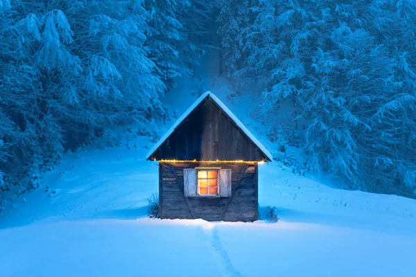 Sessiz bir ahşap kulübe, kışın sık ormanlarla çevrili, karla kaplı bir dağ çayırında tek başına duruyor. Noel kartpostalı. Karlı dağ ormanları