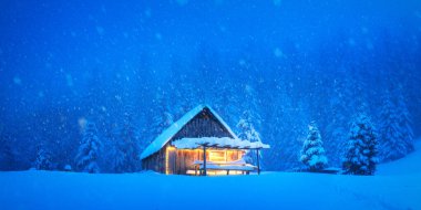 Issız dağ kulübesi, karlı bir orman çayırında kışın yemyeşil ağaçlarla kaplıydı. Noel kartpostalı. Karlı dağ ormanları