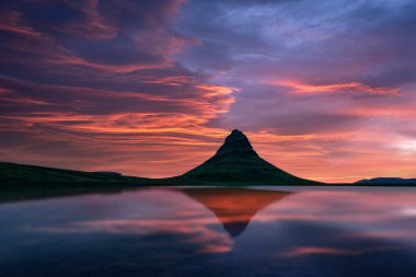 Gün batımında Kirkjufell dağının üzerindeki çarpıcı renkli gökyüzü bir dağ gölünün berrak sularına yansıyor. Kirkjufell Şelalesi, İzlanda yakınlarında muhteşem bir sabah manzarası. Peyzaj fotoğrafçılığı