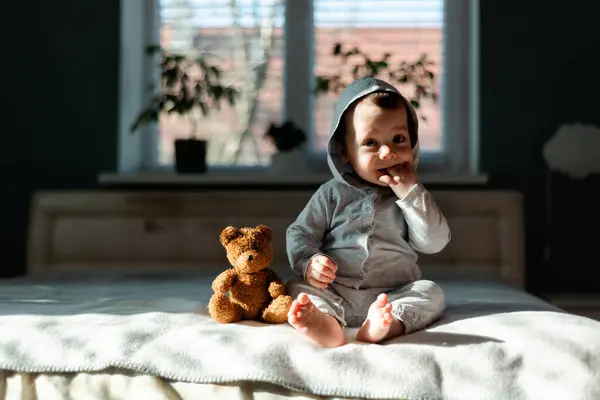 お気に入りのテディベアとベッドの上に座っている灰色のパジャマの小さな少年 幸せな子供時代のコンセプト — ストック写真